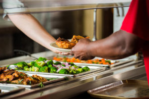 Person being handed a plate under a salad bar from an attendant.